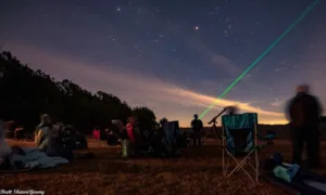 An image of the night sky at Goodale State Park with viewers star gazing. You can see lawn chairs, telescopes, and a laser pointing in to the night sky